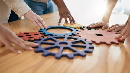 Different gear shapes fit together with diverse hands touching each