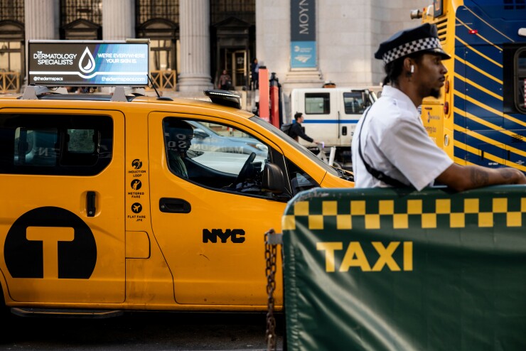 A person on a street leaning on a taxi sign outside of Penn Station in New York.