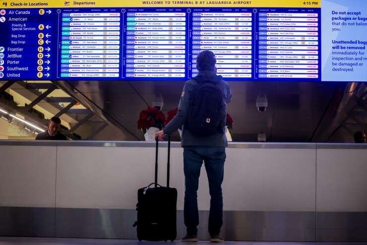 A traveler with a suitcase stands in front of a departure sign board in La Guardia airport.