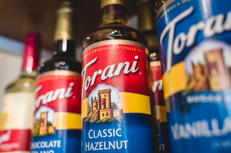 Four bottles of Torani syrup on a shelf.