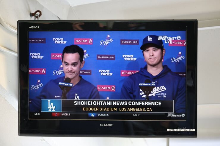 A TV in the press box shows Shohei Ohtani during a news conference at Dodger Stadium.