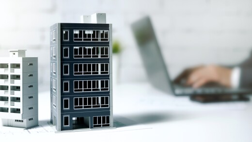 two model buildings on a desk with a person working on a laptop in the background