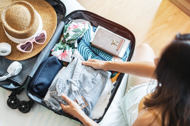A woman packing her suitcase: Her jean shorts, bathing suit, passport, sun hat, pink-heart sunglasses and white headphones are shown.