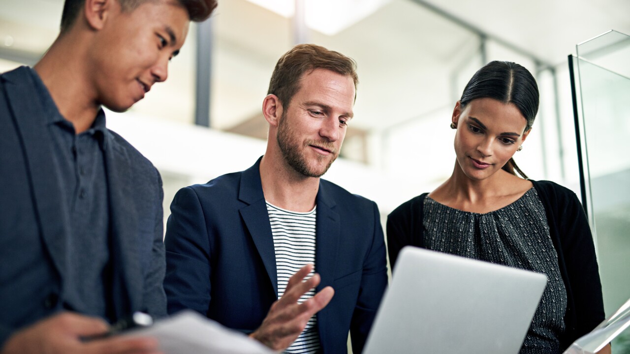Three people standing, looking at laptop