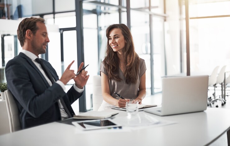 Two employees talking, one taking notes, one holding hands up to show something