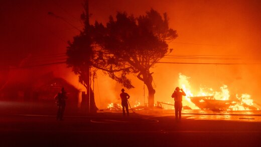 Three firefighters silhouetted against a burning structure creating an orange glow