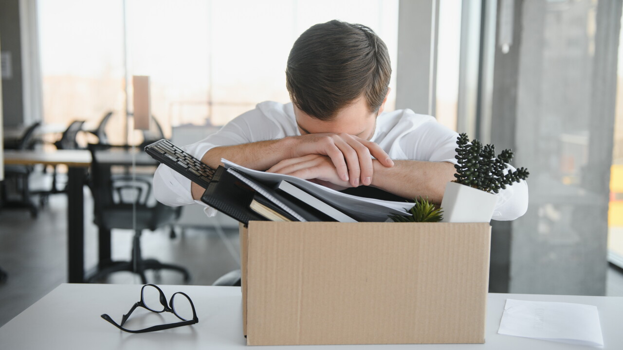Man with head on arms, box packed with desk items, fired, laid off
