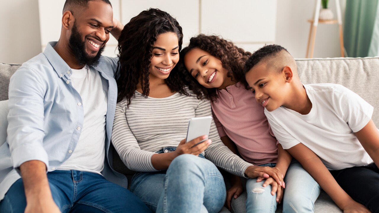 Family with two small children sitting on couch looking at smart phone