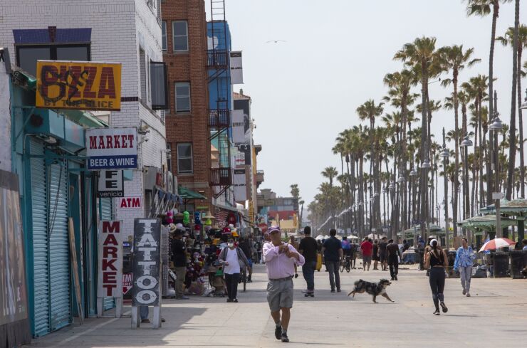 People walk along the Venice Beach boardwalk in Los Angeles, California, U.S., on Tuesday, June 15, 2021. California lifted most of its Covid-19 restrictions Tuesday as part of a grand reopening in which the state will end capacity limits, physical distancing and mask requirements for those that are vaccinated. Photographer: Jill Connelly/Bloomberg