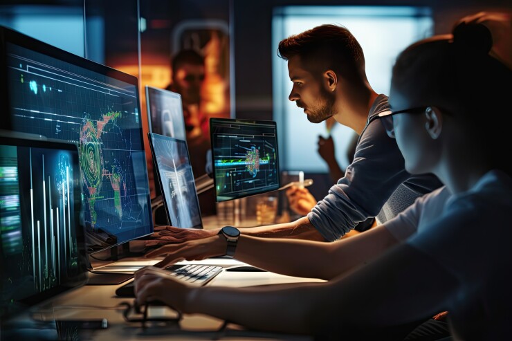 Two people looking at several computer monitors.
