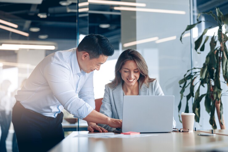Man and woman in office man helping woman at work woman typing on laptop
