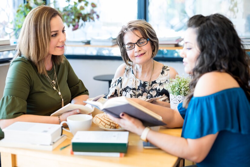 Three women looking at books sitting at table