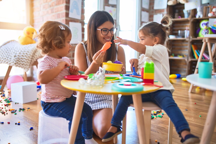 Young teacher and toddlers playing meals using plastic food and cutlery toy at kindergarten.