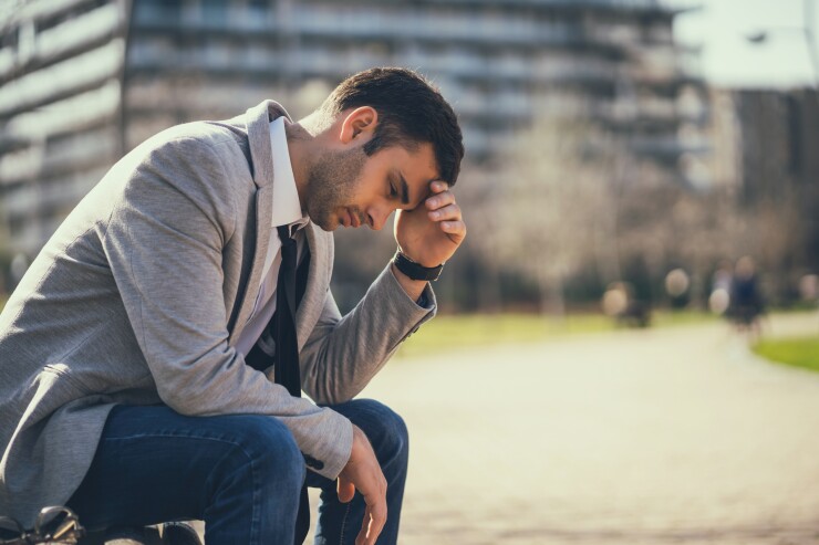 Man in suit sitting outside with head in hand, worried, sad