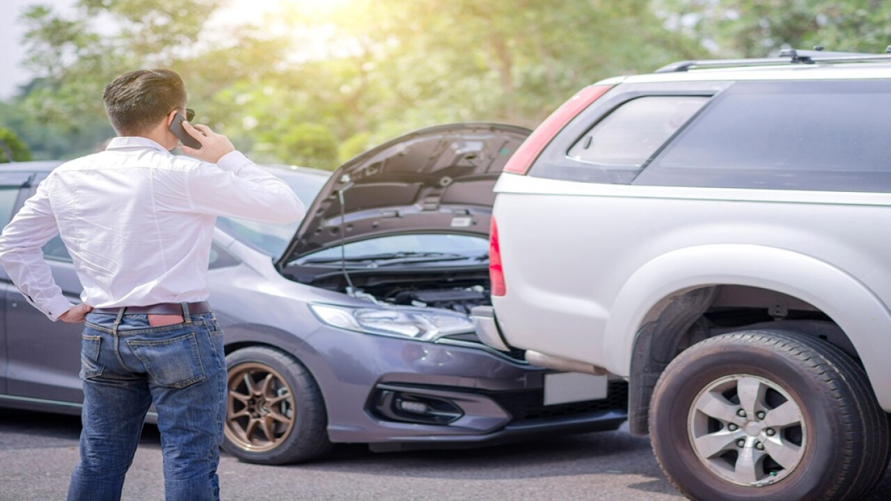 Man on a cell phone standing alongside a two-car accident.