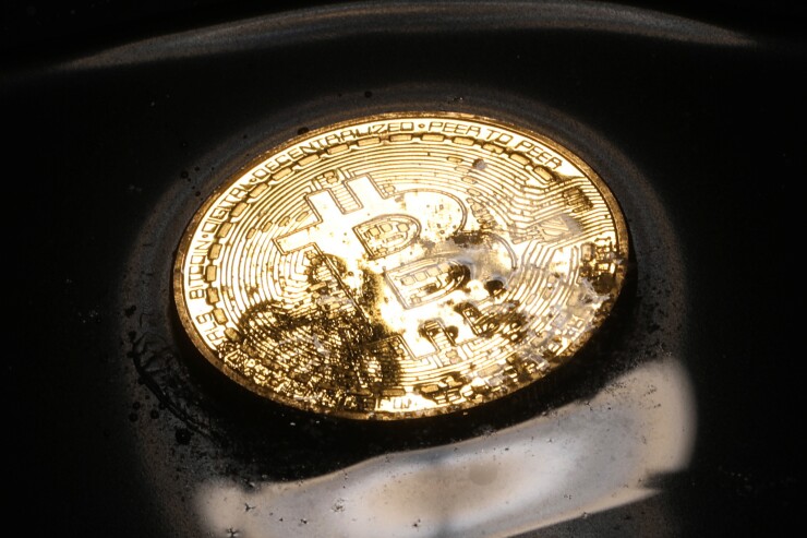 A coin representing Bitcoin cryptocurrency sits in a pool of melted ice crystals and water.