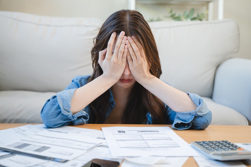 Person with hands over eyes surrounded by bills.