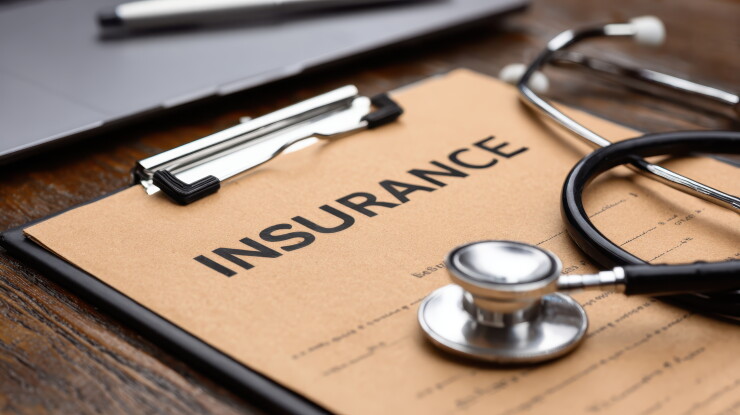 Medical stethoscope resting on brown insurance clipboard near laptop, highlighting healthcare expenses and medical documentation process.