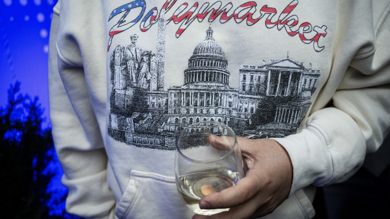 A picture of a person holding a drink and wearing a Polymarket sweatshirt with images of Washington, D.C., on it.