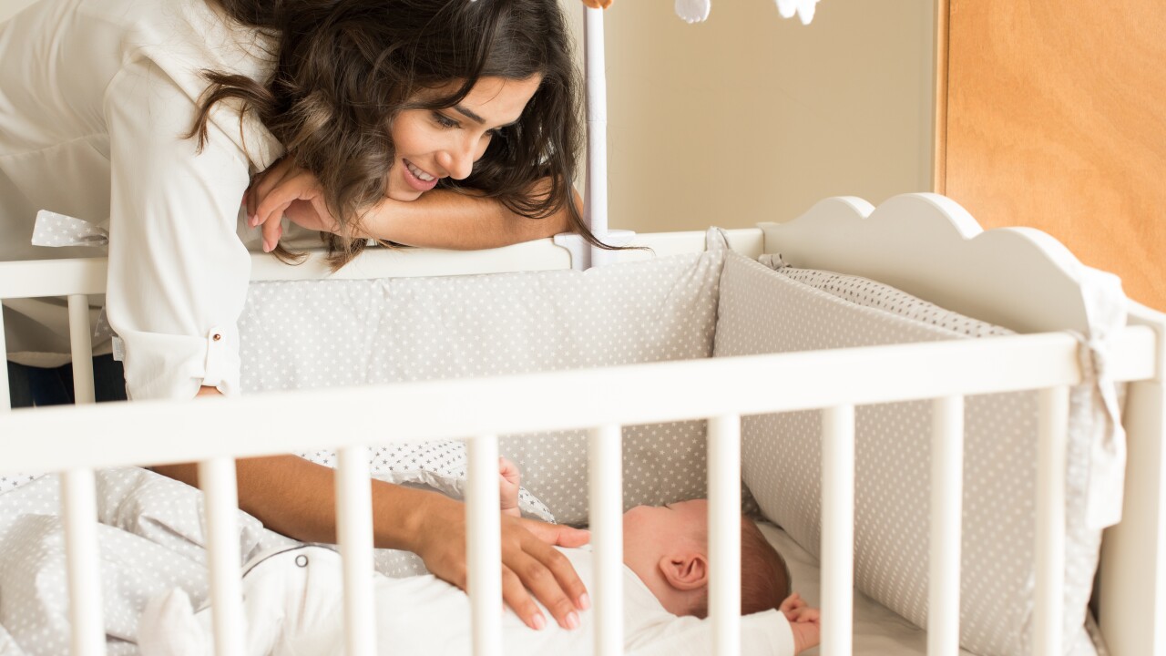 Mother leaning over crib, smiling, baby sleeping