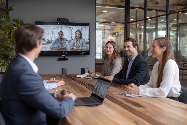 Group of employees sitting at conference table, hybrid meeting with employees on screen