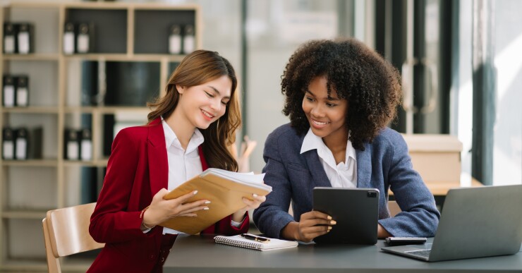 Two women in office working on tablet and with paperwork