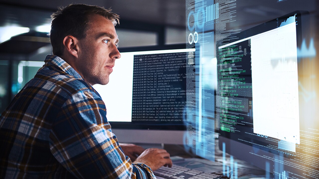 A person looking at two monitors with a holographic image of code.