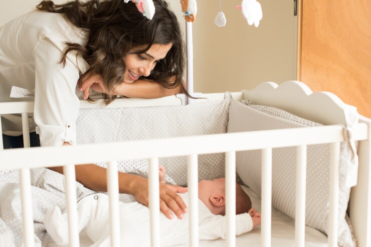 Mother leaning over crib, smiling, baby sleeping