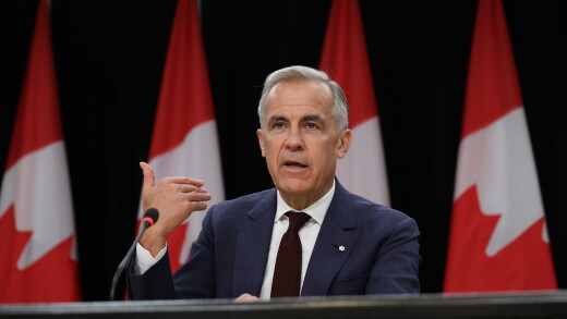 Mark Carney, Canada's prime minister speaking, with Canadian flags behind him