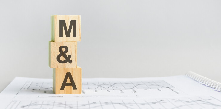 Wooden block with words M&A for mergers and acquisitions. M&A wooden blocks on a paper with a gray background business concept