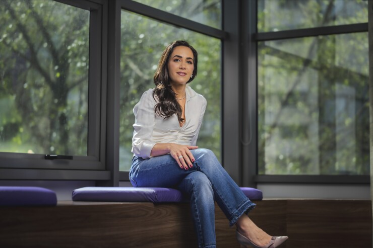 Nubank co-founder and U.S. CEO Cristina Junqueira sits on a purple cushioned bench and poses for a headshot.