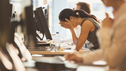 Stressed businesswoman with head in hands at office desk.