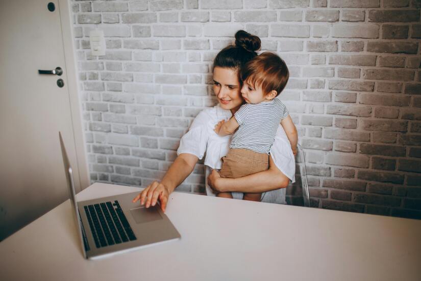 Woman holding her baby while typing on the computer