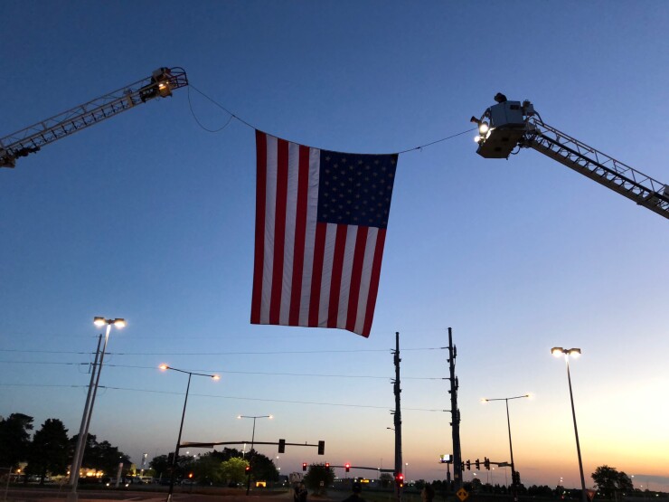 Two ladder trucks from the local fire department hoisted a giant American flag above the entrance to the parking lot for participants taking part in placing flags on grave sites at Fort Snelling National Cemetery prior to Memorial Day 2018.