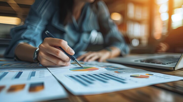 A woman writing on a sheet of paper filled with charts.