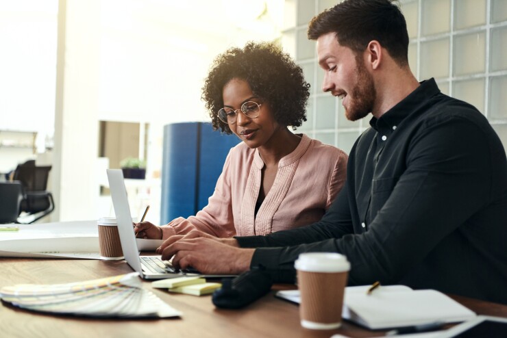Two people working together in office, looking at laptop