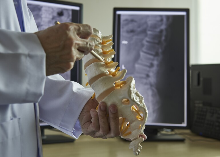 A neurosurgeon pointing at lumbar vertebra model in medical off