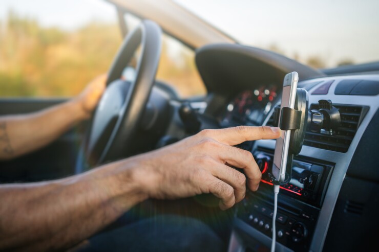 A person driving with one hand on the wheel while using a phone that is mounted to an air vent.