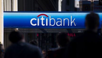 Pedestrians walk under signage at a Citibank branch in San Francisco.