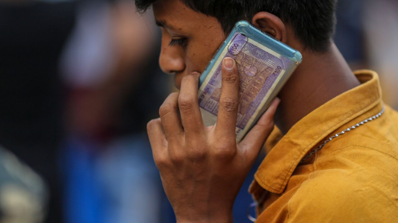 A man uses a mobile phone holding a one hundred Indian rupee banknote in Hyderabad, India, on Wednesday, March 23, 2022. India’s urban consumption is driving recovery from late pandemic wave but has further intensified the divergence between cities and the hinterland, according to a report by Citigroup Inc released last week. Photographer: Dhiraj Singh/Bloomberg