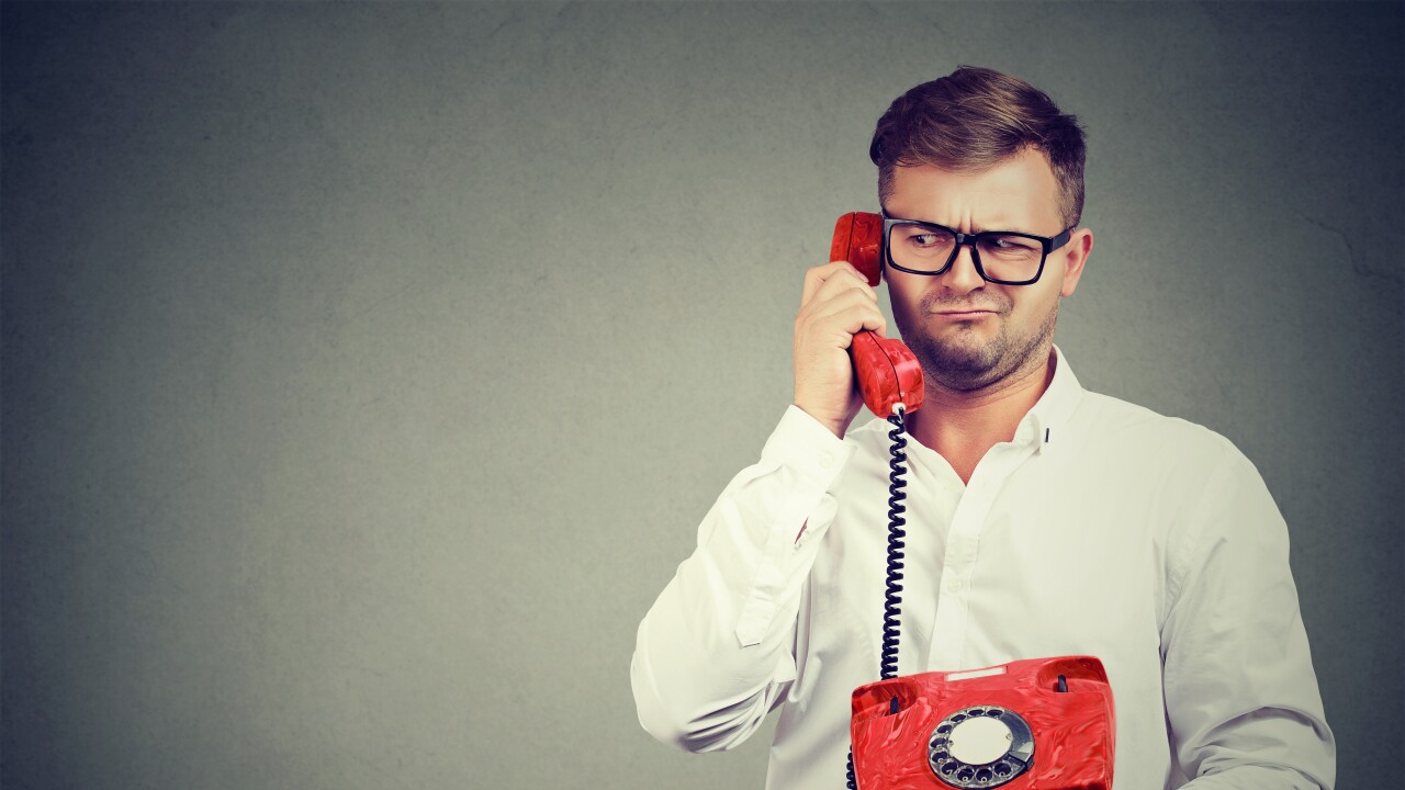 Casual man in eyeglasses talking on old-fashioned phone looking away in misunderstanding.