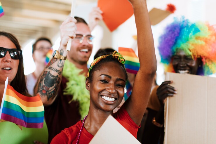 A group of people waving pride flags, smiling and looking off to the distance.