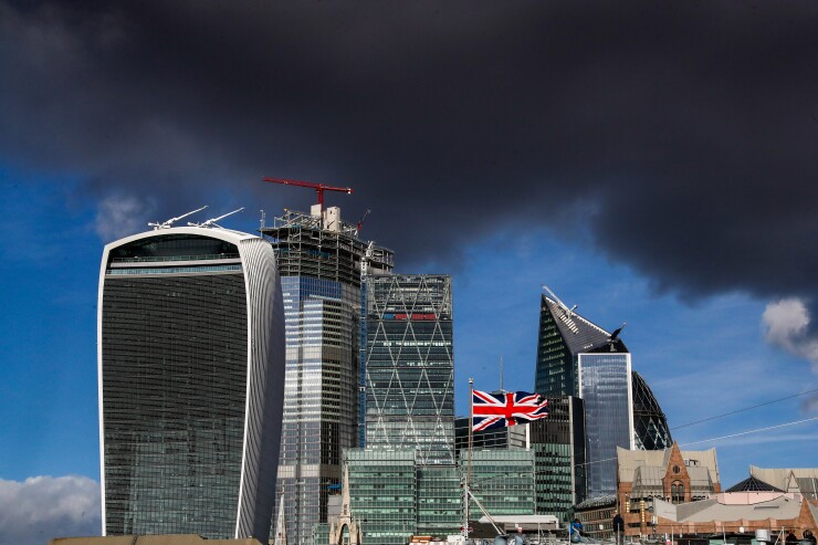 A Union Flag flies from the mast of a vessel docked in the River Thames in front of skyscrapers in London.