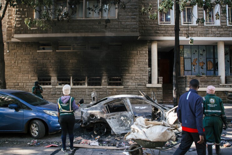 City cleaners look at a burnt-out vehicle following anti-government protests in Nairobi.