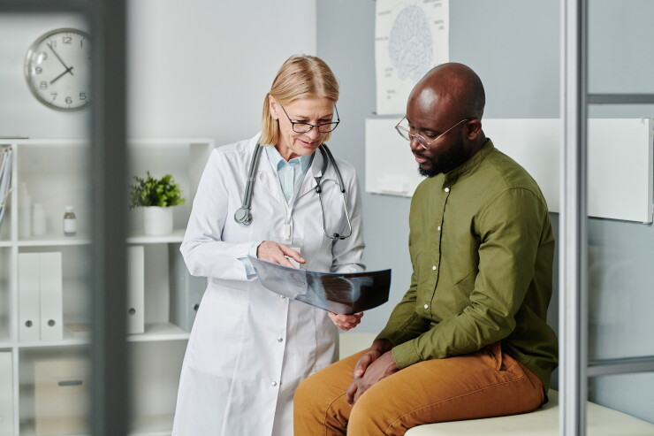 Young adult man wearing glasses and green shirt speaking with female doctor