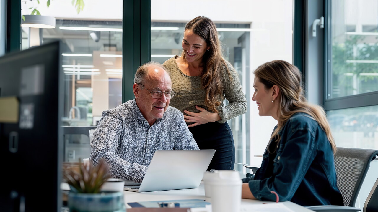 Two women and a man professionally collaborating at a table using a computer.