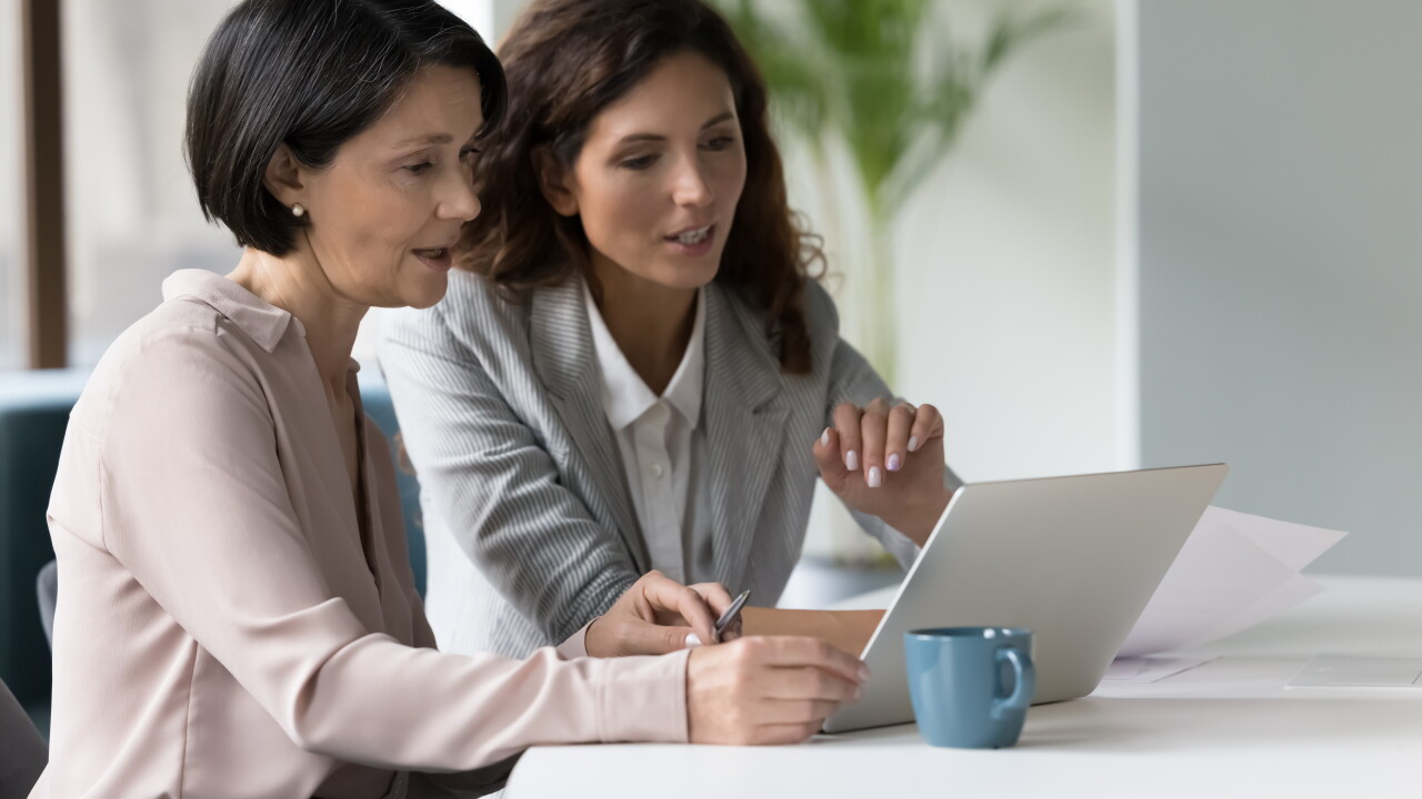 Two businesswomen discuss app or on-line presentation using laptop