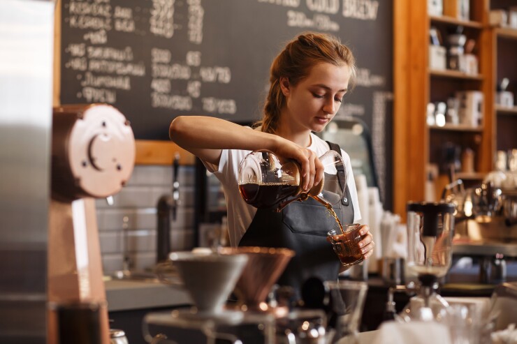 A woman pours coffee into a glass cup behind a cafe counter.