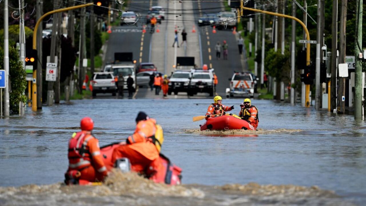 People in life rafts on a flooded road with cars in the background.