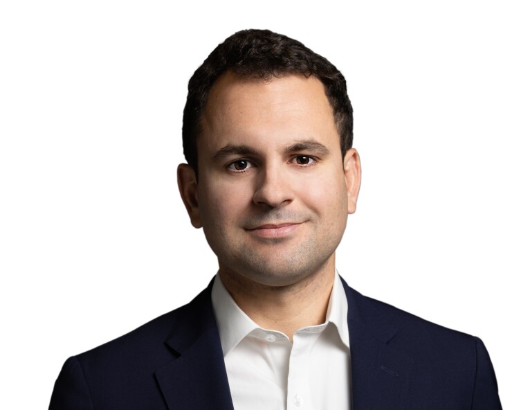 Headshot of Will Peck, a man with short dark hair, wearing a navy blazer and white collared shirt against a white background.